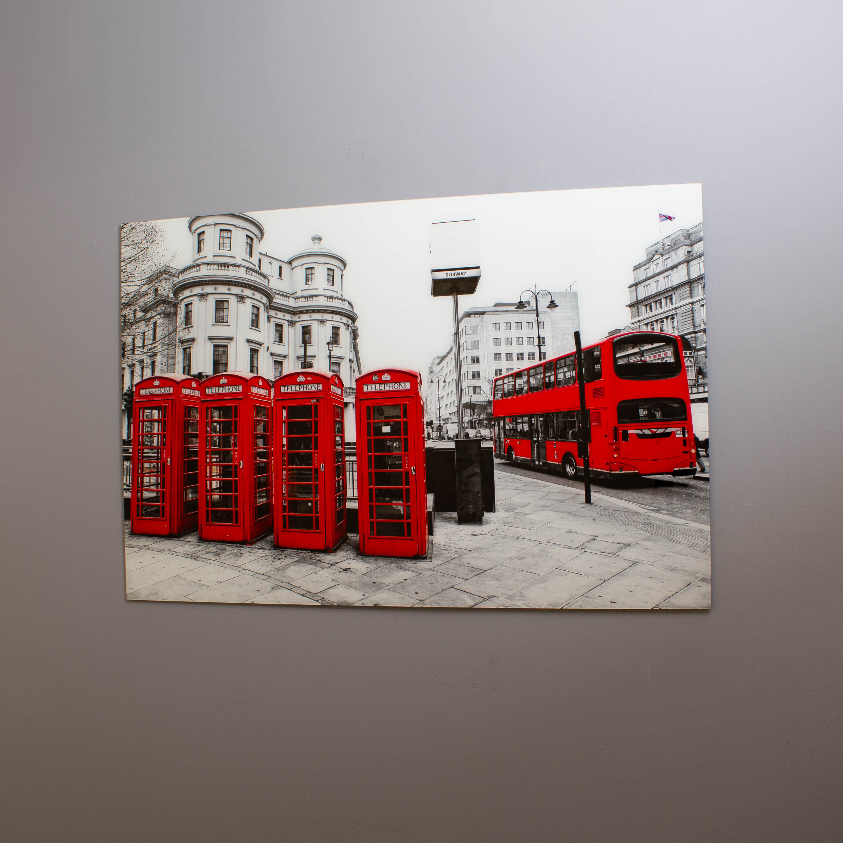 A tempered glass wall art featuring a high-resolution print of red telephone boxes and a bus on a street, with a high-gloss finish.